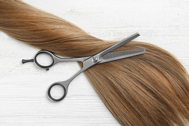 Photo of Flat lay composition with light brown hair and thinning scissors on white wooden background. Hairdresser service