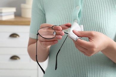 Photo of Woman wiping her glasses with microfiber cloth at home, closeup