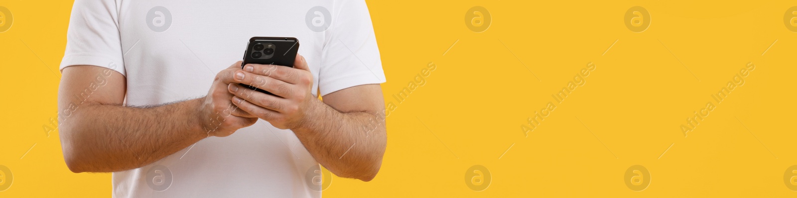 Image of Man typing message on mobile phone against yellow background, closeup. Banner design with space for text