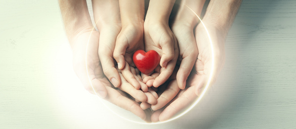 Image of Family holding small red heart in hands on wooden background, top view. Banner design 