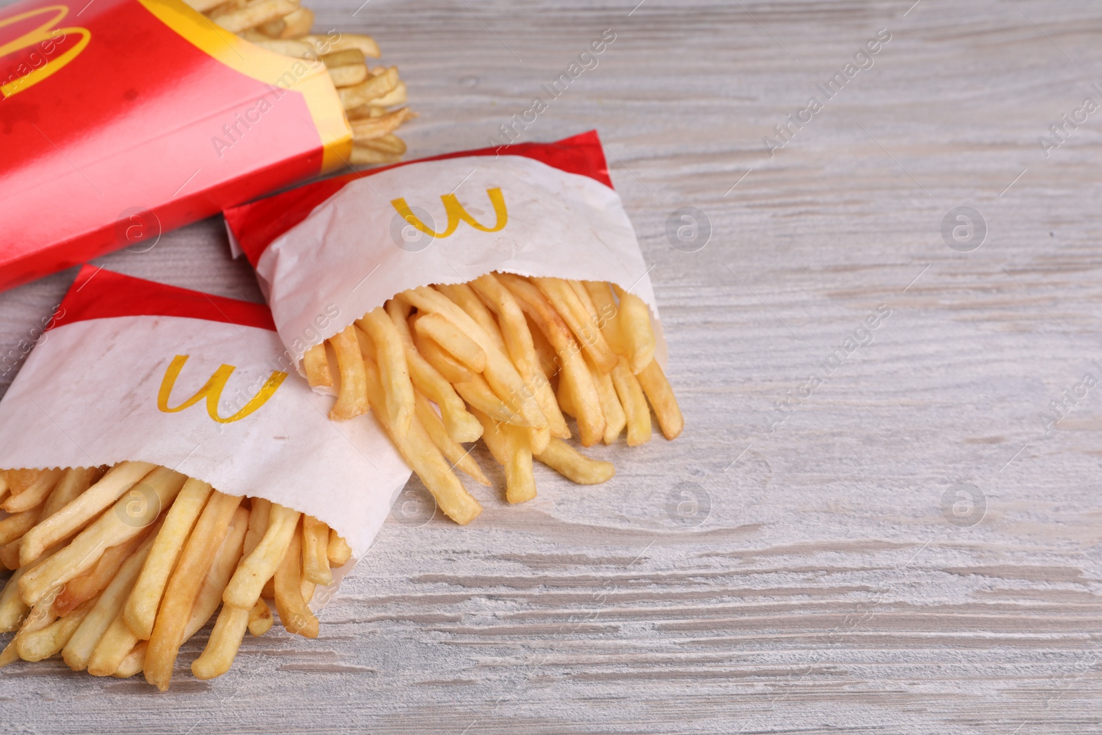 Photo of MYKOLAIV, UKRAINE - AUGUST 12, 2021: Small and big portions of McDonald's French fries on white wooden table, space for text