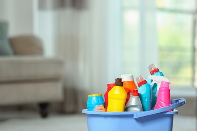 Plastic bucket with different cleaning products indoors, space for text