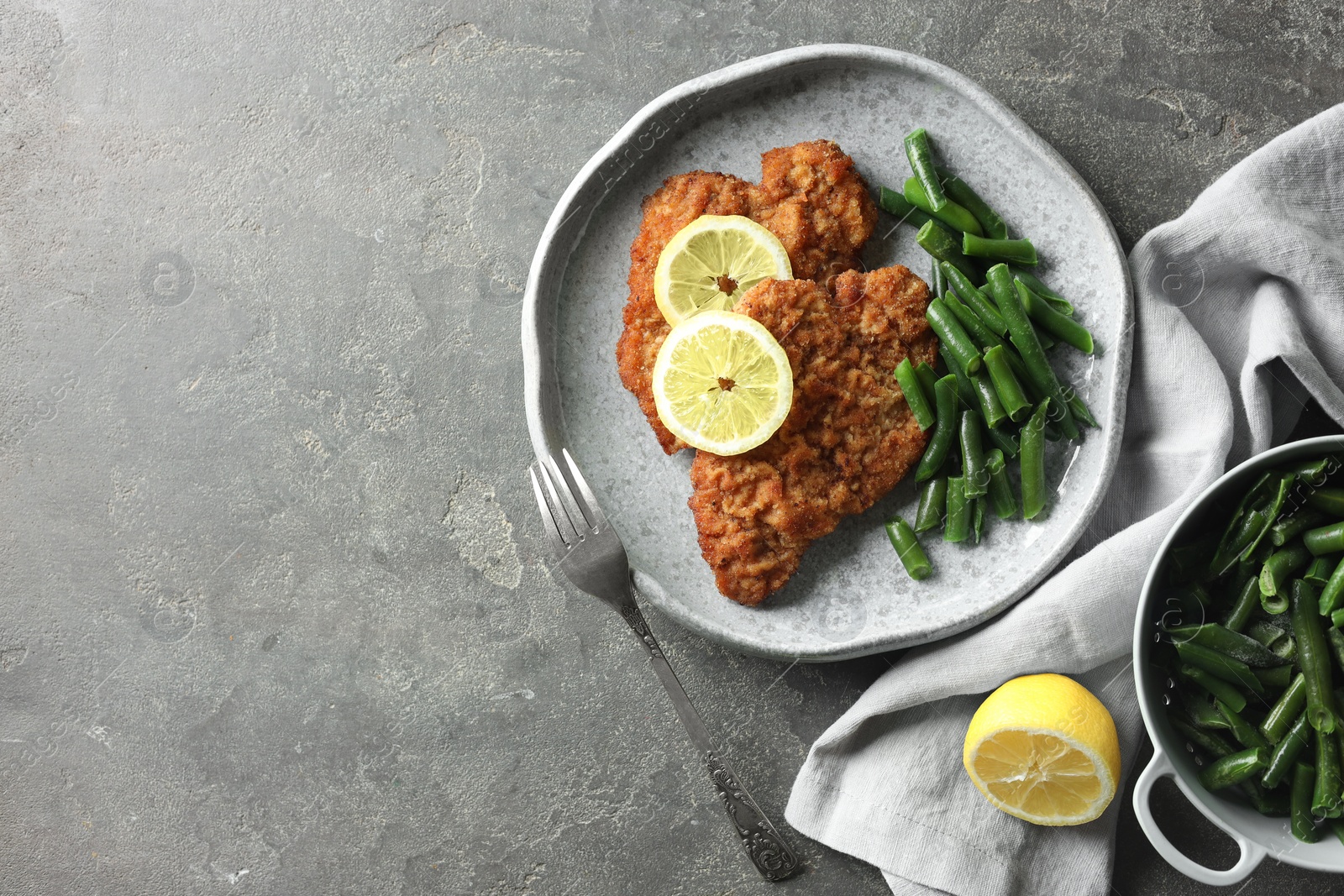 Photo of Tasty schnitzels served with lemon and green beans on grey table, flat lay. Space for text