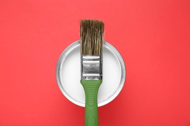 Can of white paint with brush on red background, top view