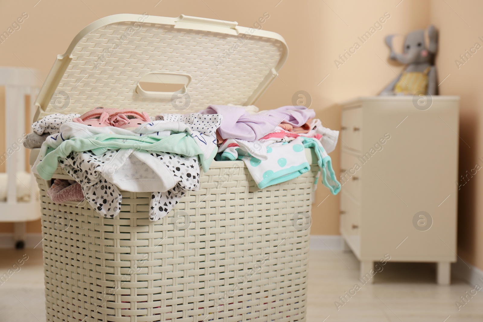 Photo of Laundry basket with baby clothes in child room, closeup