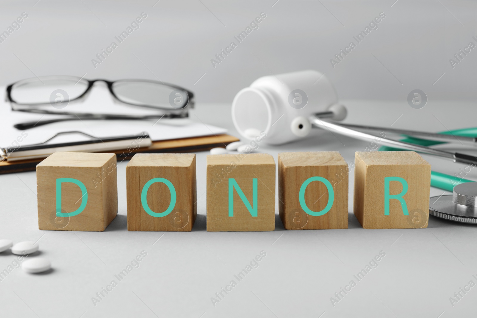Photo of Word Donor made of wooden cubes, clipboard, pills and stethoscope on light grey table