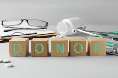 Word Donor made of wooden cubes, clipboard, pills and stethoscope on light grey table