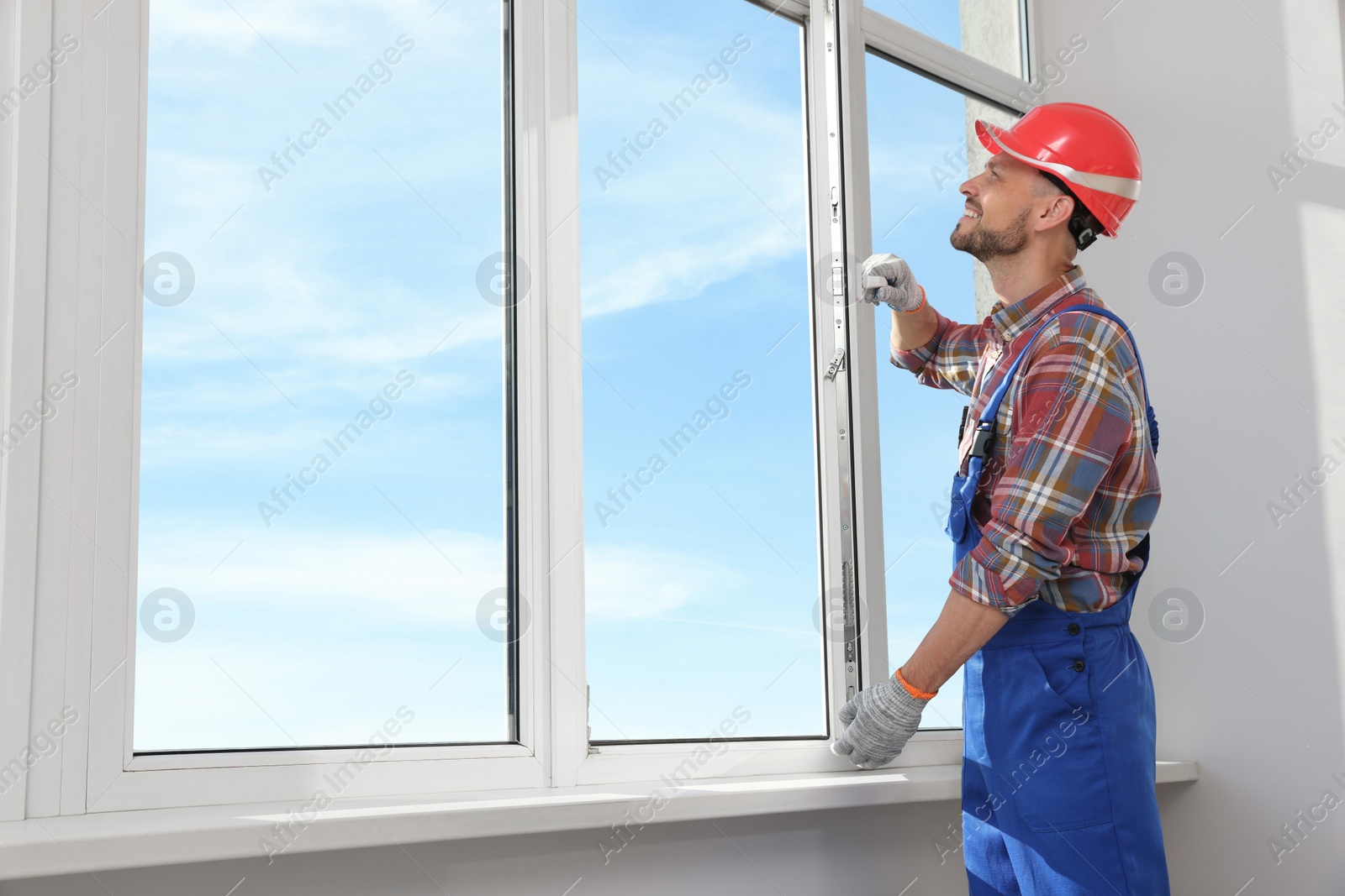 Photo of Worker in uniform installing plastic window indoors