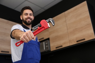 Photo of Male plumber holding pipe wrench in kitchen, space for text. Repair service