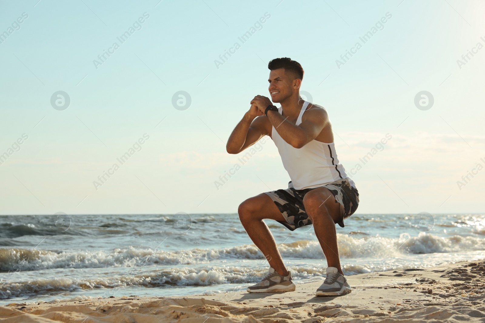 Photo of Sporty man doing exercise on sandy beach at sunset