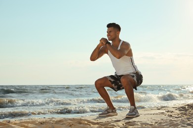 Photo of Sporty man doing exercise on sandy beach at sunset