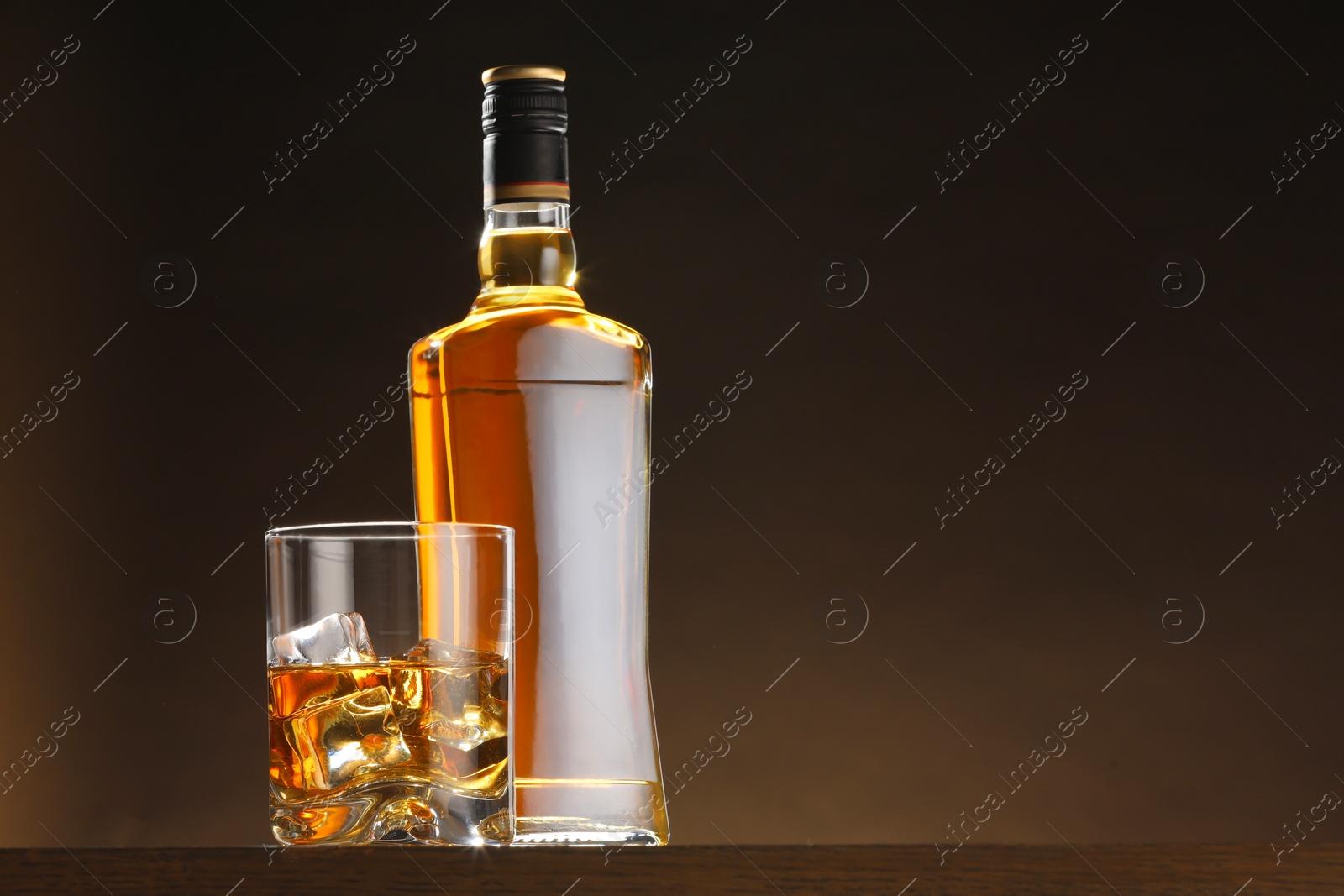 Photo of Whiskey with ice cubes in glass and bottle on table, space for text