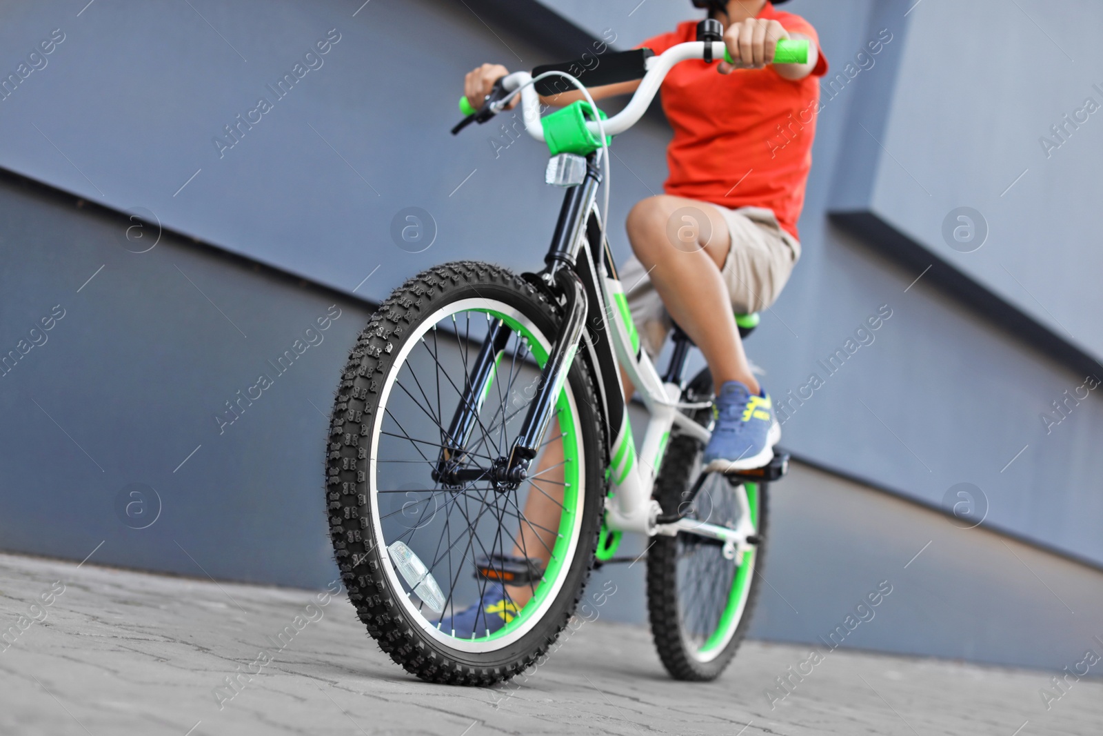 Photo of Little boy riding bicycle on street near gray wall, closeup