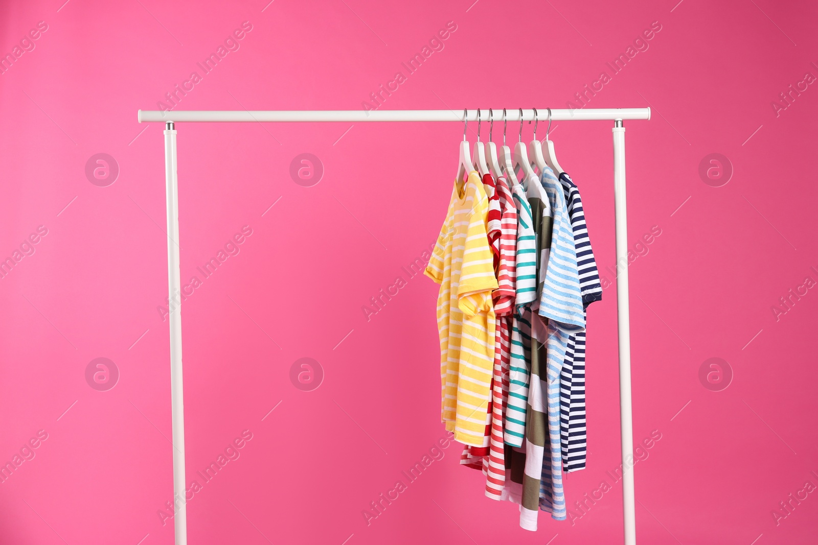 Photo of Colorful clothes hanging on rack against pink background