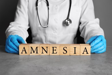 Photo of Doctor holding cubes with word Amnesia at light grey table, closeup