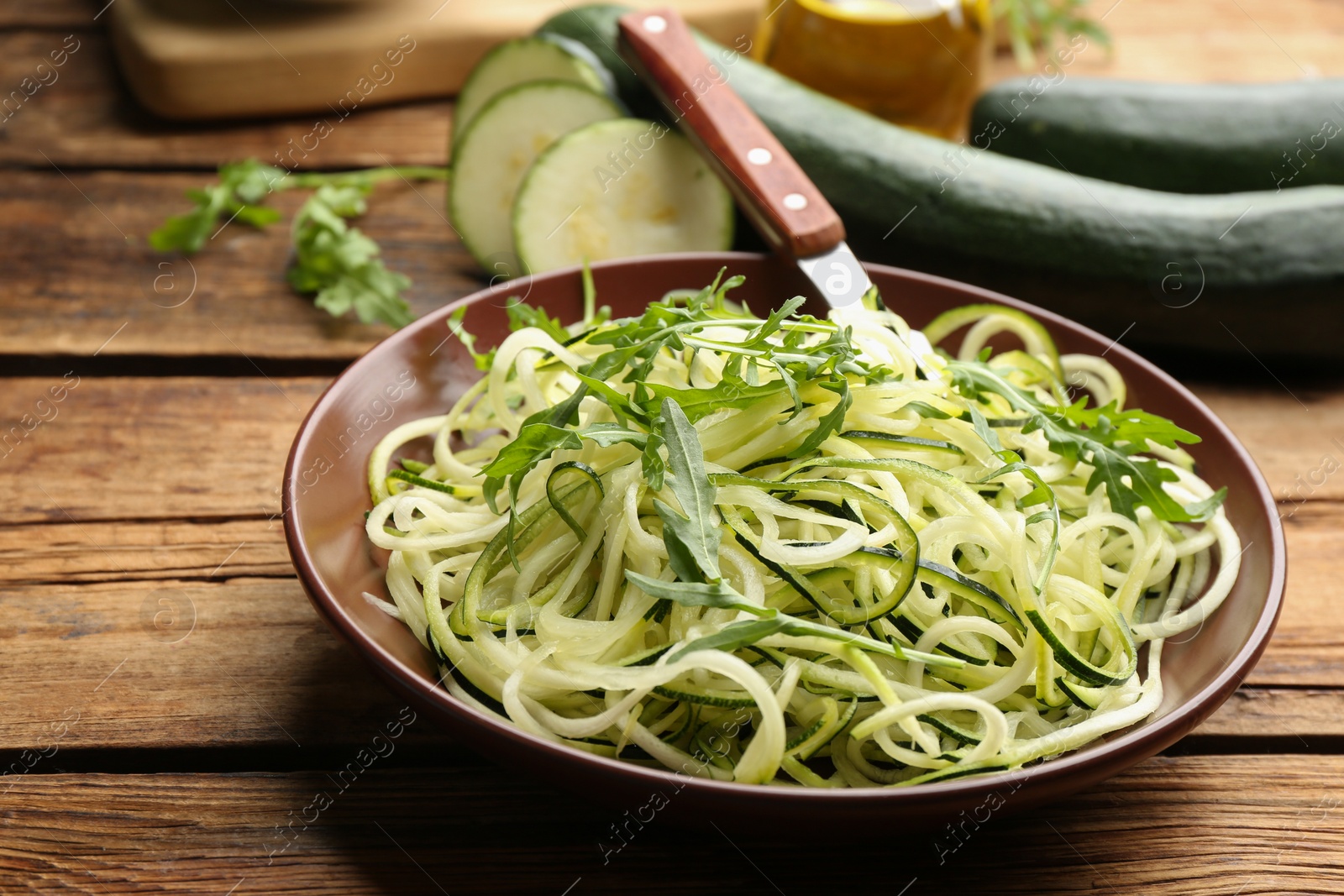 Photo of Tasty zucchini pasta with arugula on wooden table