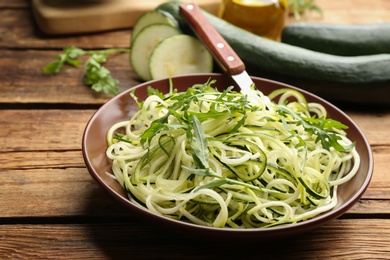 Photo of Tasty zucchini pasta with arugula on wooden table