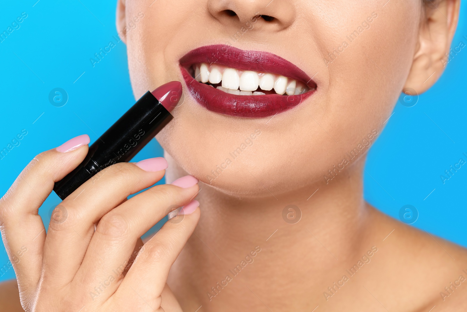 Photo of Young woman applying lipstick on color background, closeup