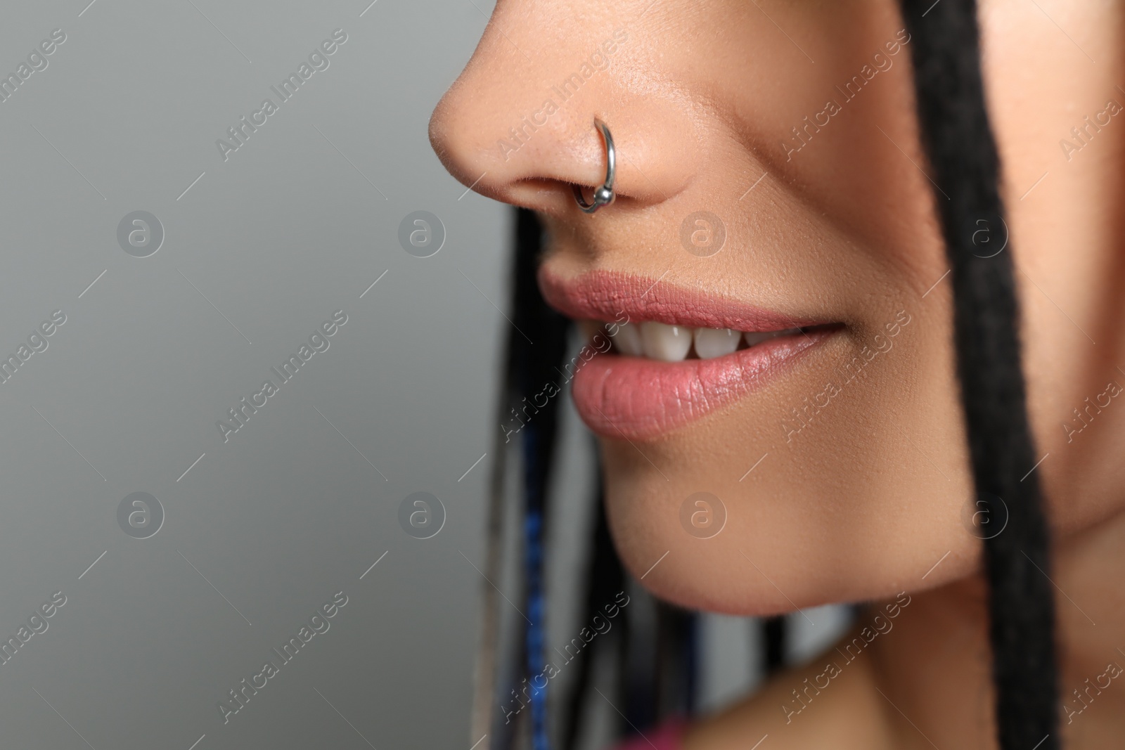 Photo of Young woman with nose piercing on grey background, closeup
