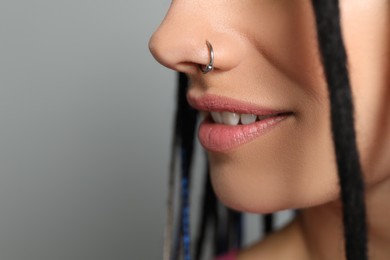 Young woman with nose piercing on grey background, closeup