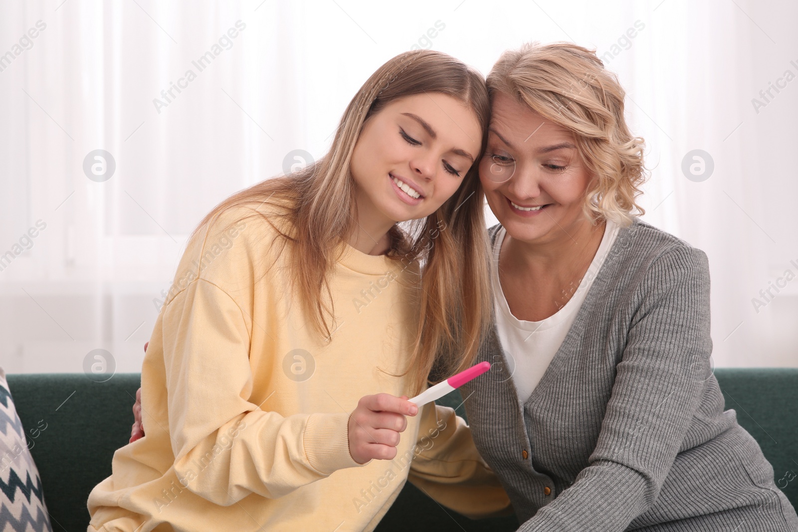 Photo of Young woman showing her mother pregnancy test at home. Grandparent reaction to future grandson