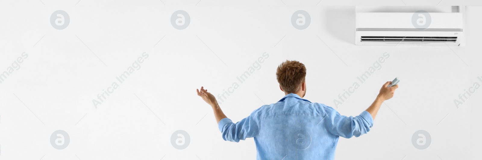 Image of Young man operating air conditioner with remote control indoors, space for text. Banner design
