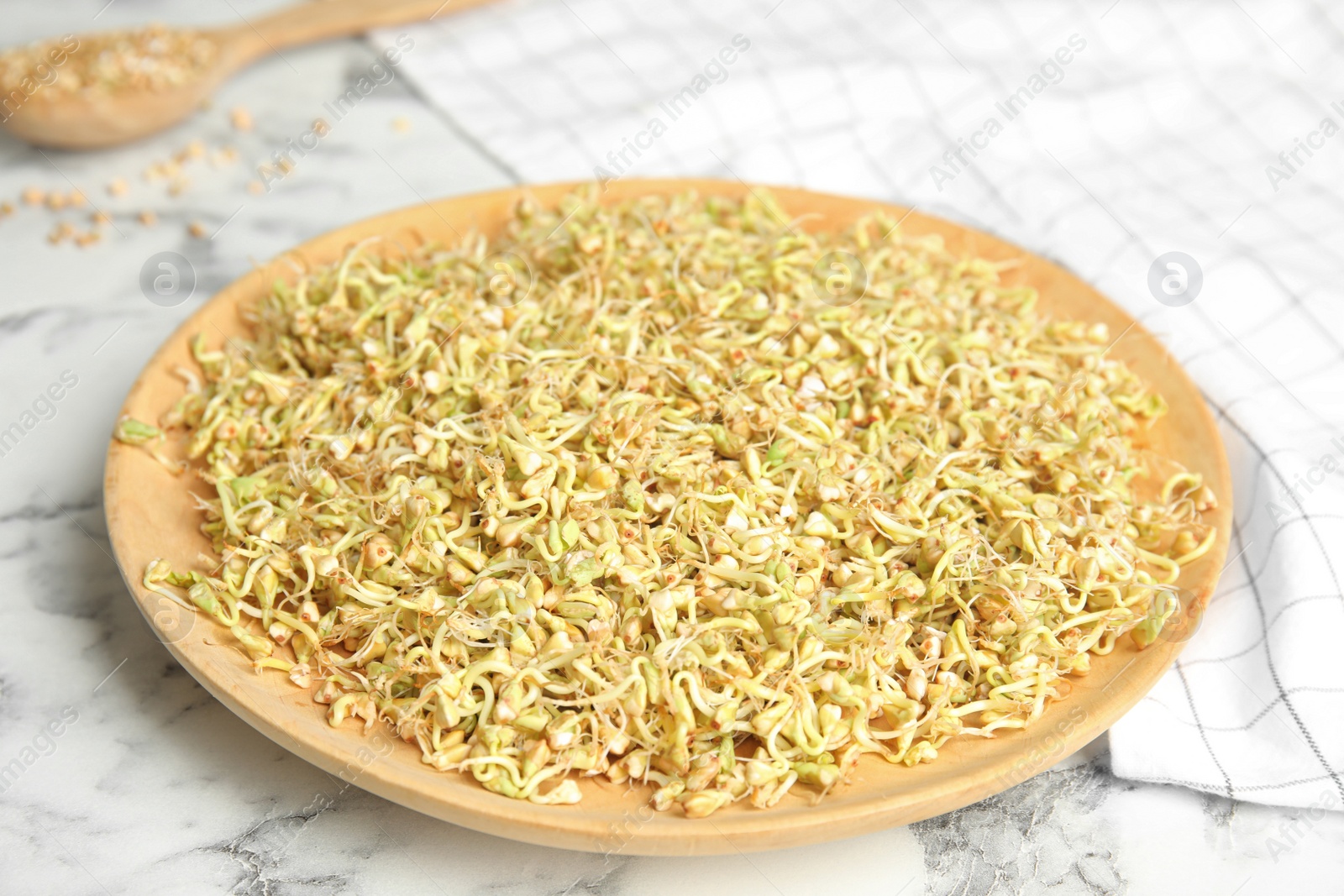 Photo of Wooden plate of sprouted green buckwheat on white marble table