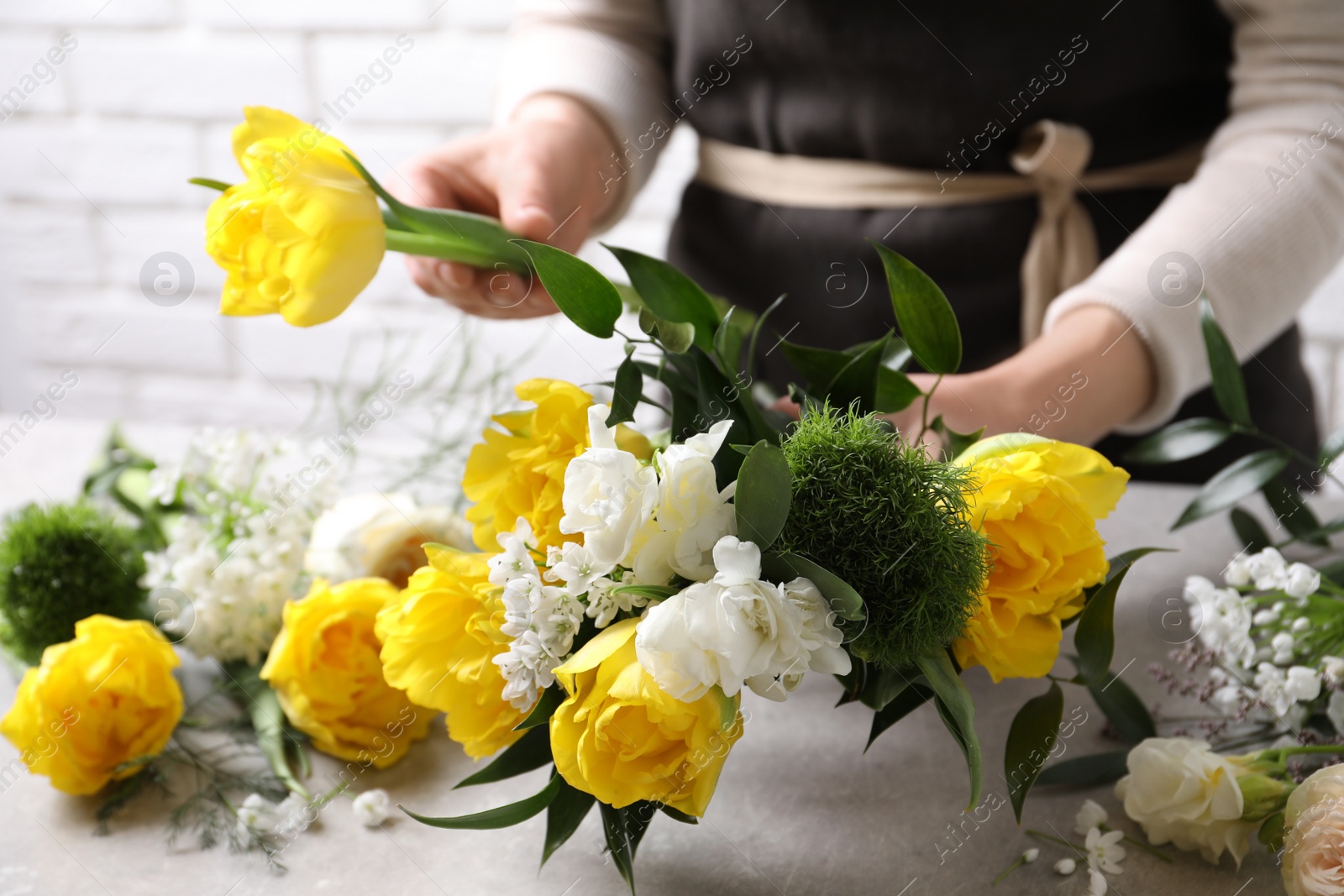 Photo of Florist making beautiful bouquet at grey table, closeup