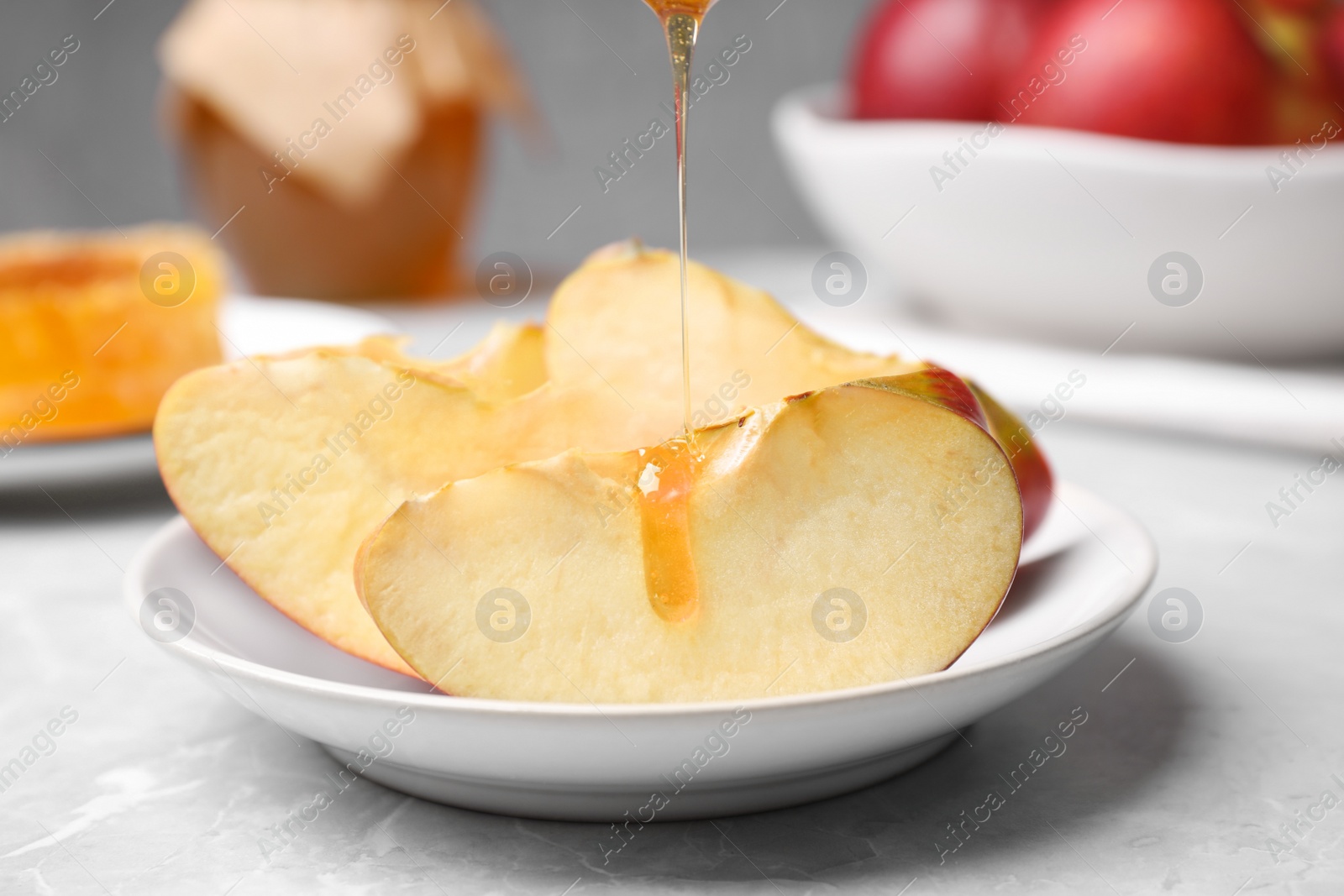 Photo of Pouring liquid honey onto apple slices on light grey marble table, closeup. Rosh Hashanah holiday