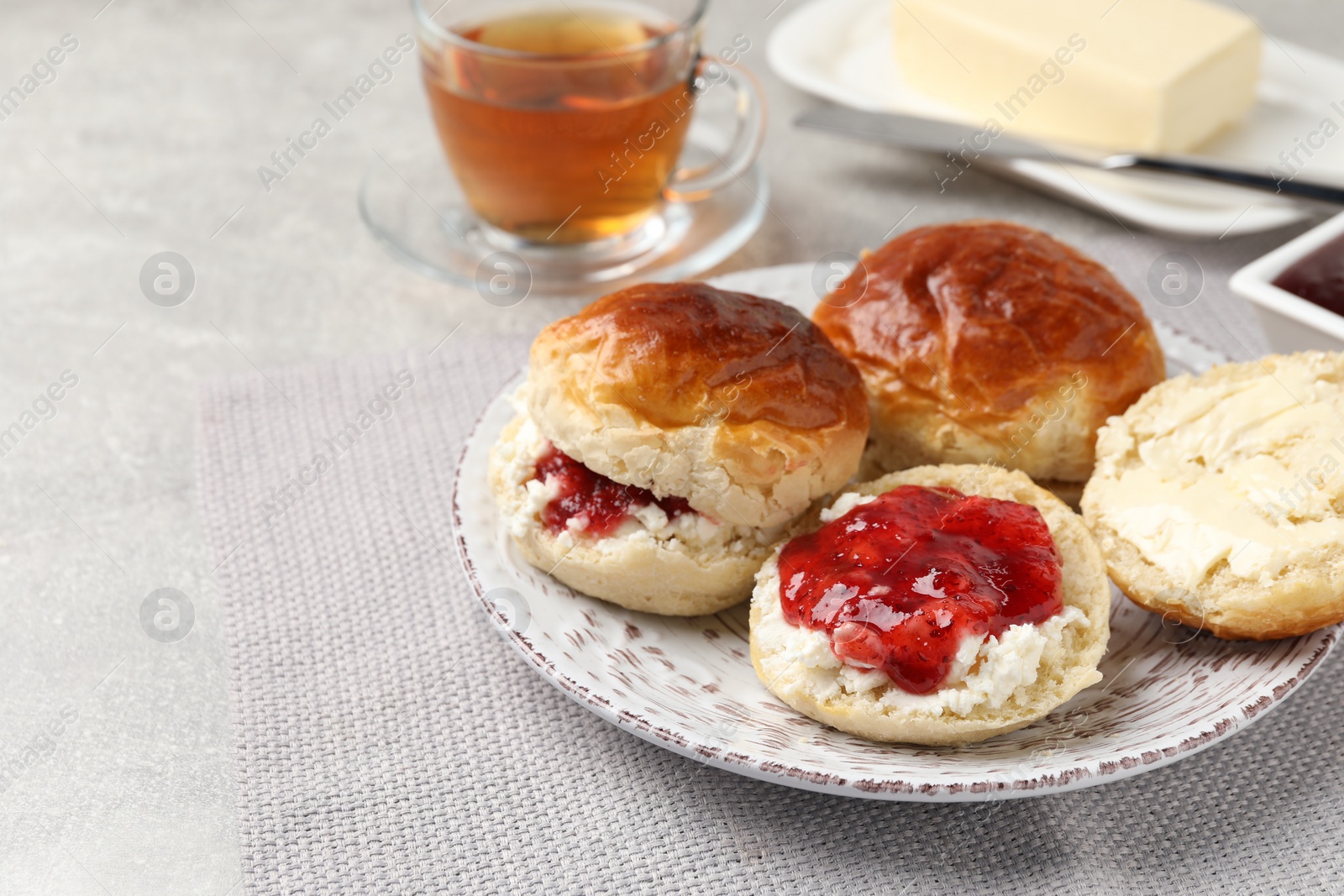 Photo of Freshly baked soda water scones with cranberry jam, butter and cup of tea on light grey mat. Space for text