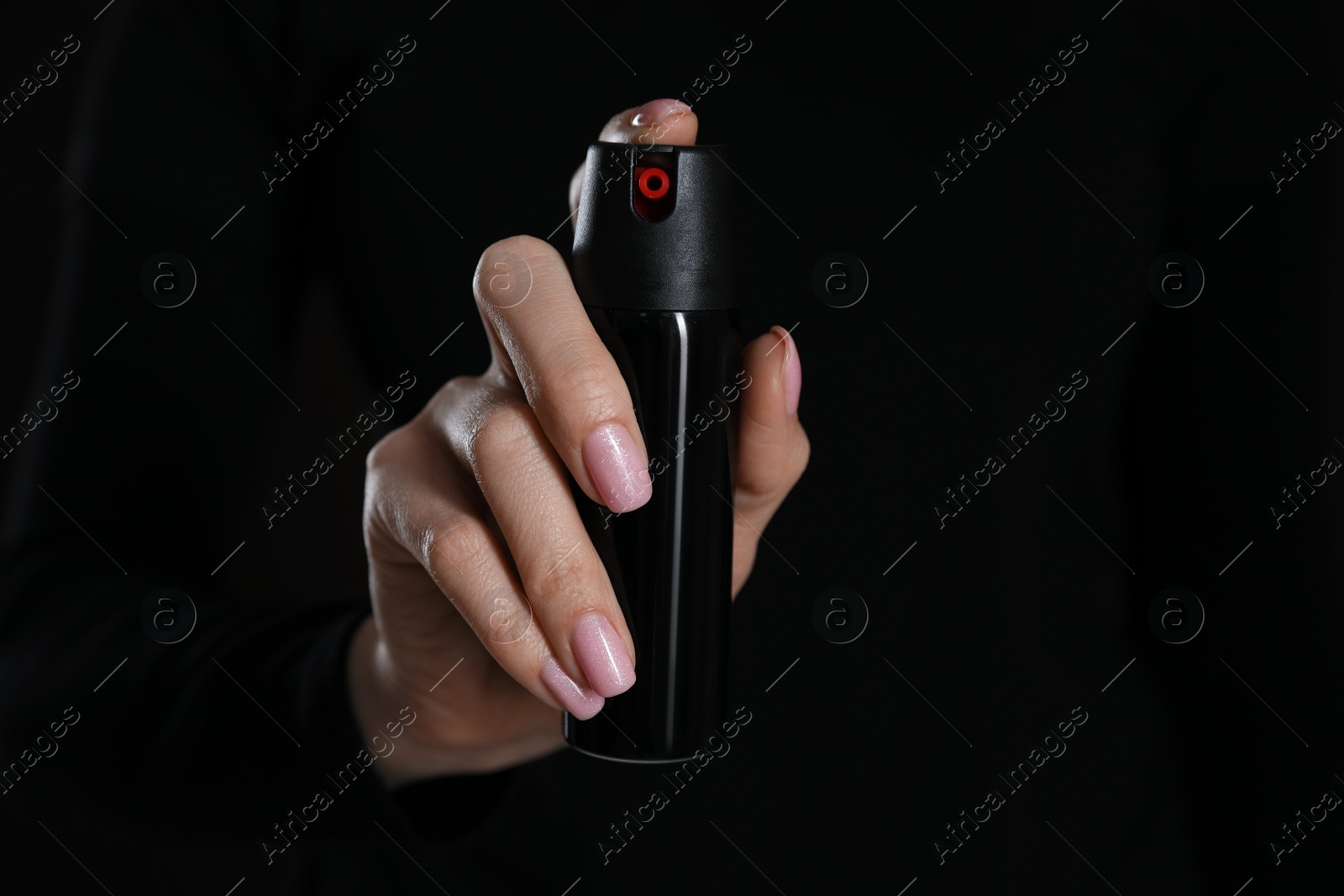 Photo of Young woman using pepper spray on black background, closeup