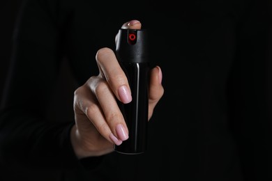 Photo of Young woman using pepper spray on black background, closeup