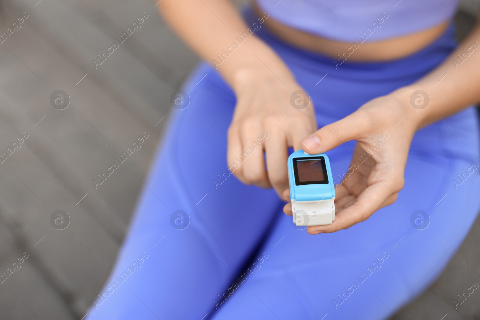 Photo of Woman checking pulse with blood pressure monitor on finger after training outdoors, closeup. Space for text