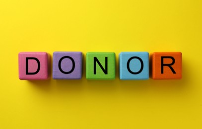 Word Donor made of colorful wooden cubes on yellow background, top view
