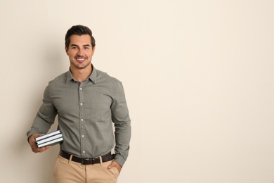 Photo of Young male teacher with books on beige background. Space for text