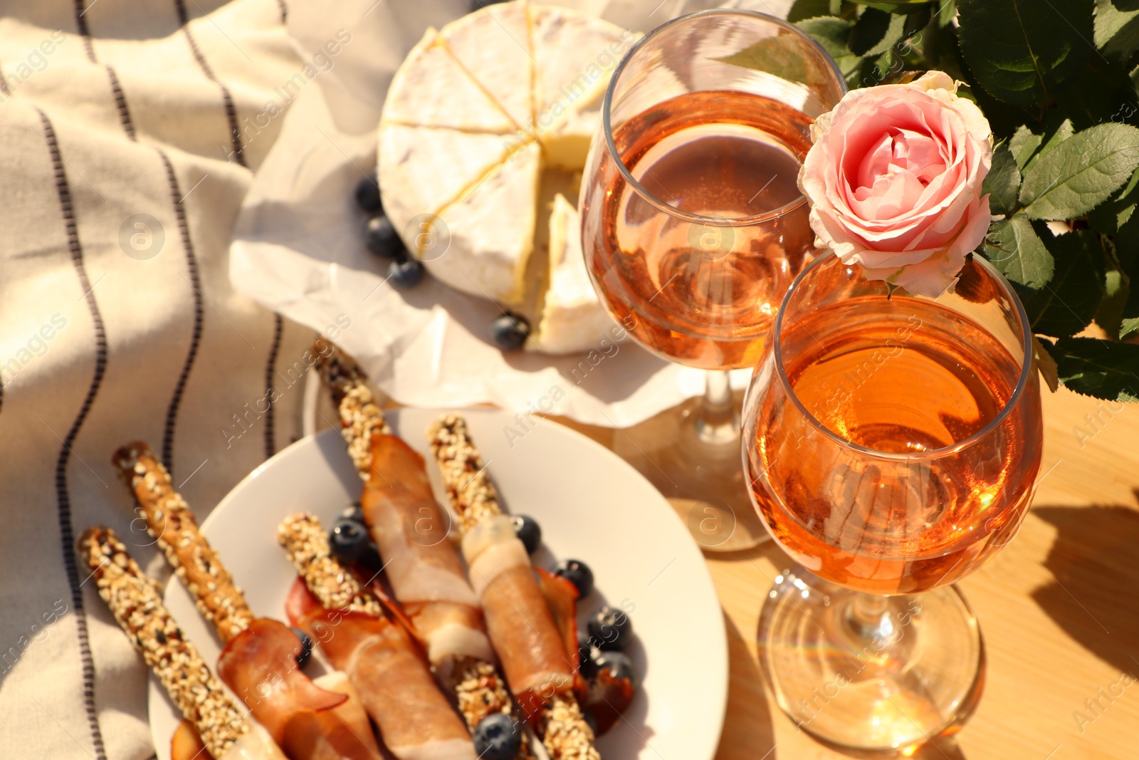 Photo of Glasses of delicious rose wine, flower and food on white picnic blanket