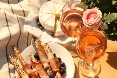 Glasses of delicious rose wine, flower and food on white picnic blanket