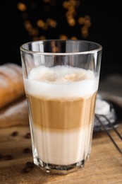 Photo of Delicious latte macchiato, croissant and coffee beans on wooden table, closeup