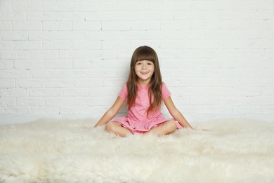 Photo of Cute little girl sitting on fur rug against brick wall