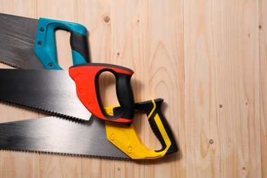 Photo of Saws with colorful handles on wooden background, flat lay. Space for text