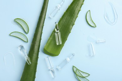 Flat lay composition with skincare ampoules and aloe leaves on light blue background