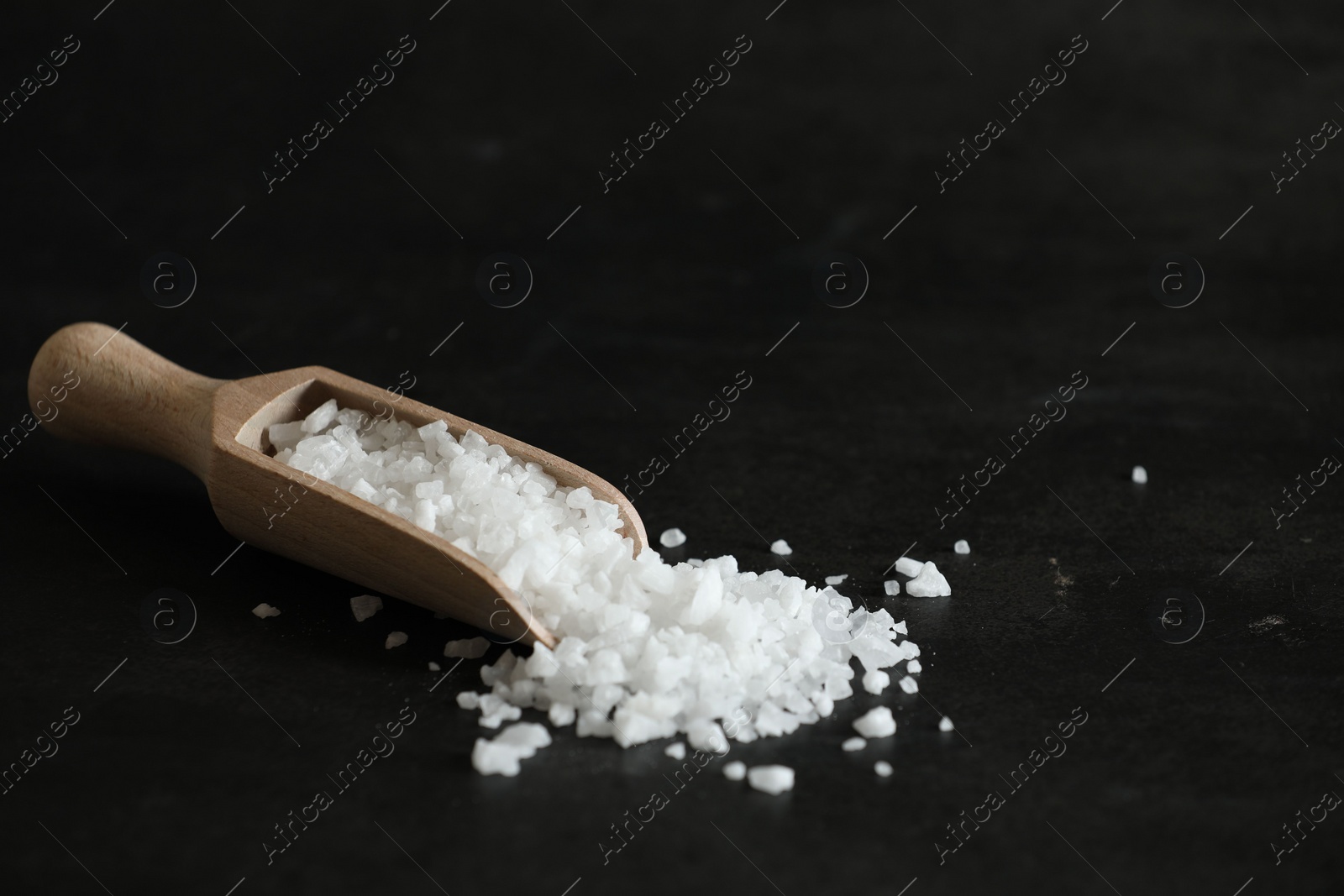 Photo of Organic salt and wooden scoop on black table. Space for text