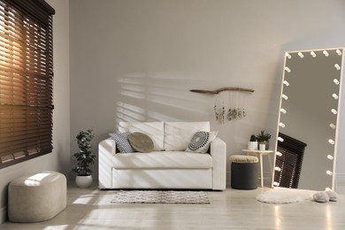 Stylish mirror with light bulbs and comfortable sofa in living room. Interior design