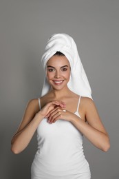Beautiful young woman with towel applying cream on hand against grey background