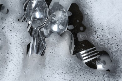 Washing silver spoons, forks and knives in water with foam, flat lay