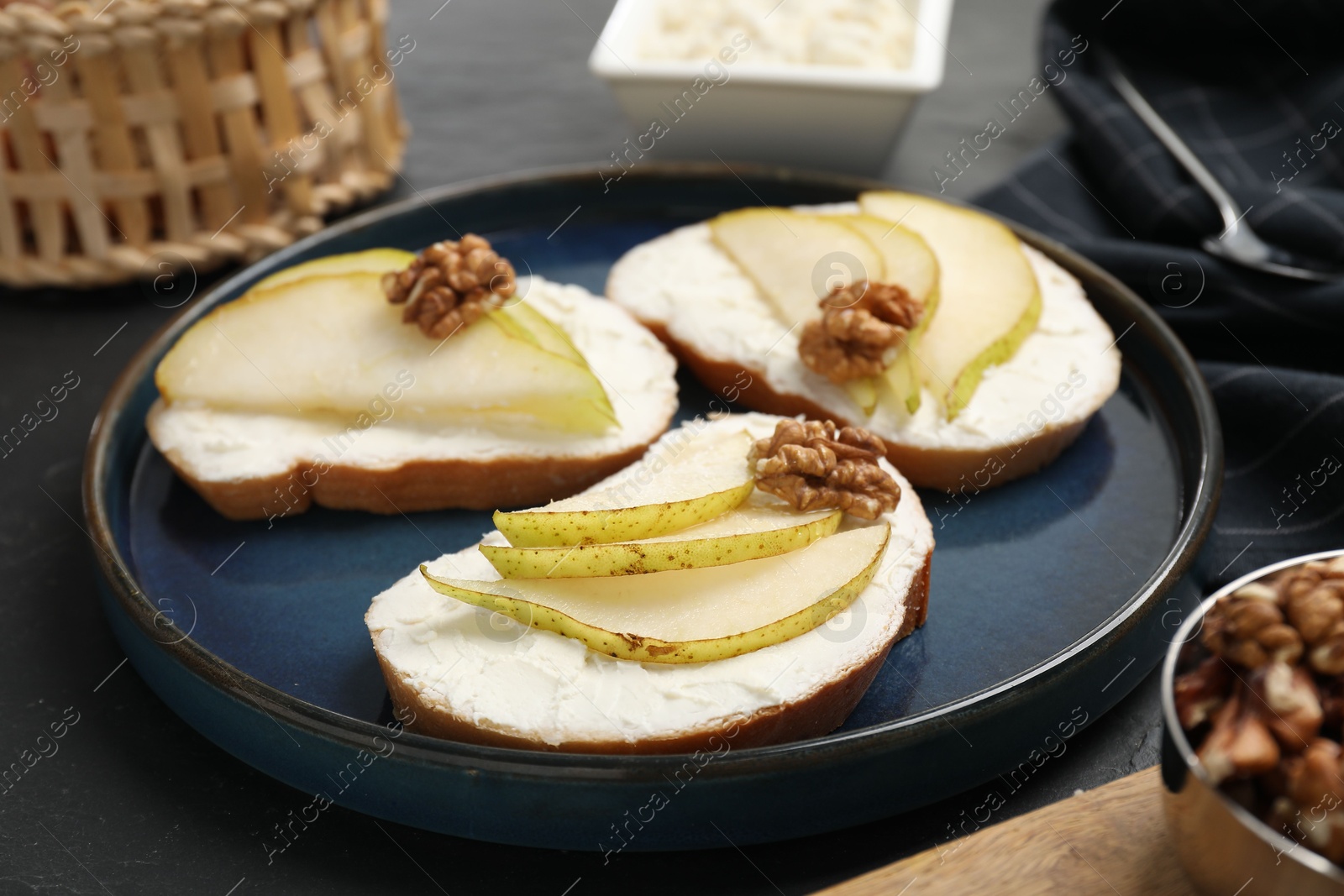 Photo of Delicious bruschettas with ricotta cheese, pears and walnuts on dark table, closeup