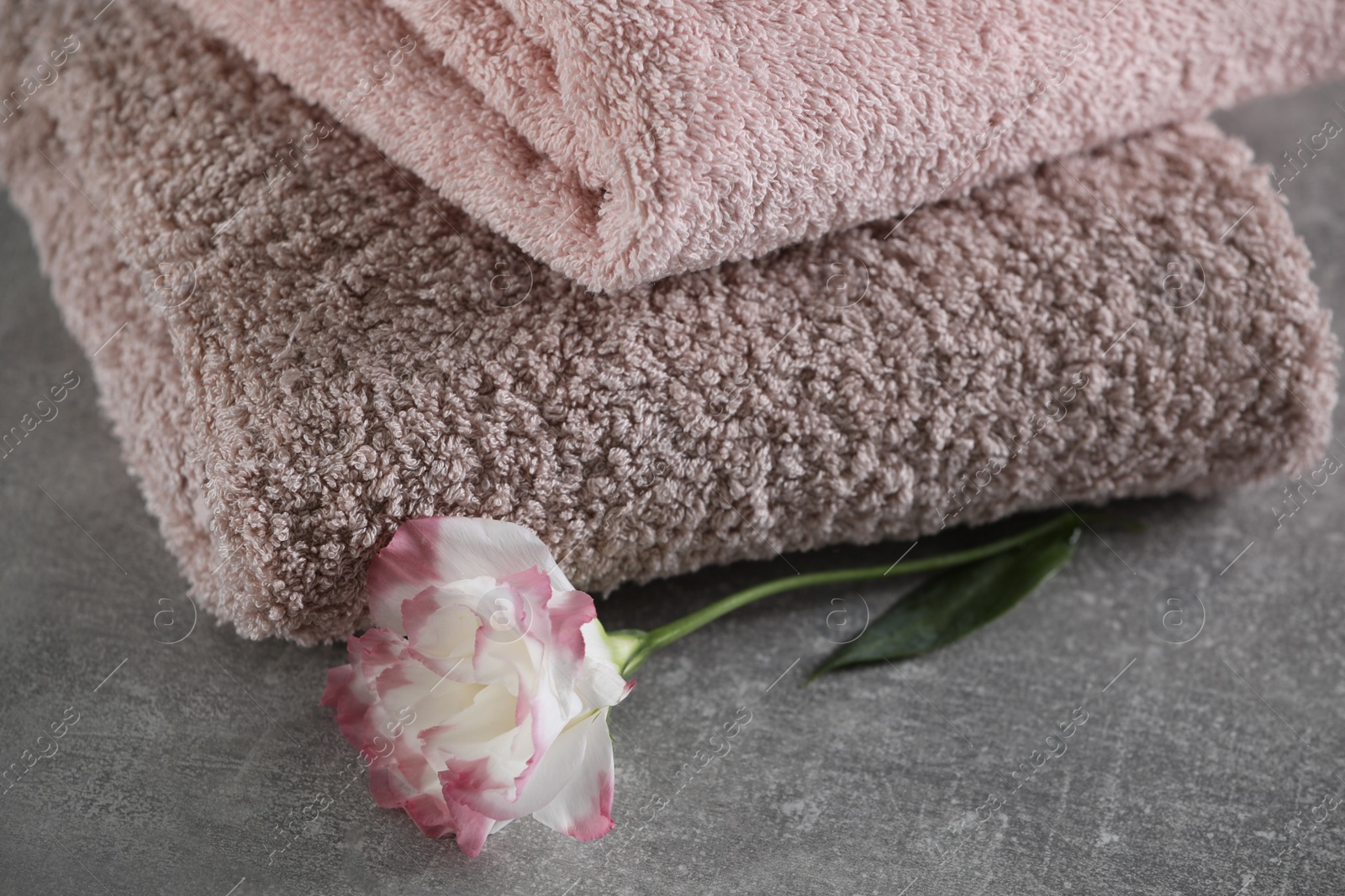 Photo of Folded soft towels with flower on grey table, closeup