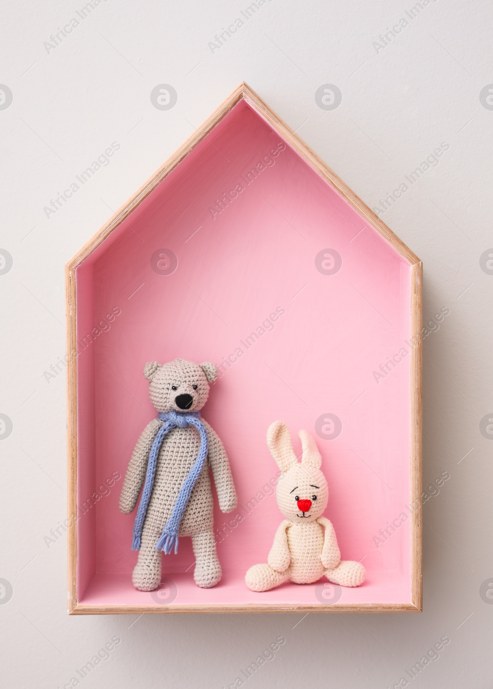 Photo of Stylish house shaped shelf with toys on white wall. Baby room interior design