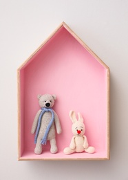 Photo of Stylish house shaped shelf with toys on white wall. Baby room interior design