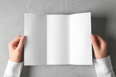 Photo of Woman holding blank brochure mock up on light background, top view